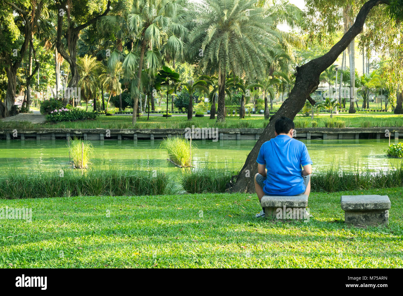 Asian man fatigués assis sur un banc en pierre après l'exercice en cours de jogging dans le parc de la ville. Banque D'Images