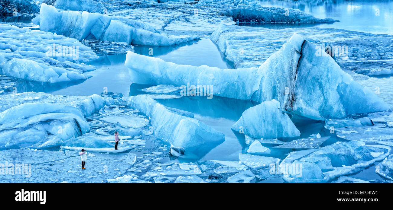 Lagune glaciaire du Jökulsárlón panorama à l'aube, en Islande. Les touristes non identifiables à pied sur la glace mince de photographier les icebergs spectaculaires. Banque D'Images