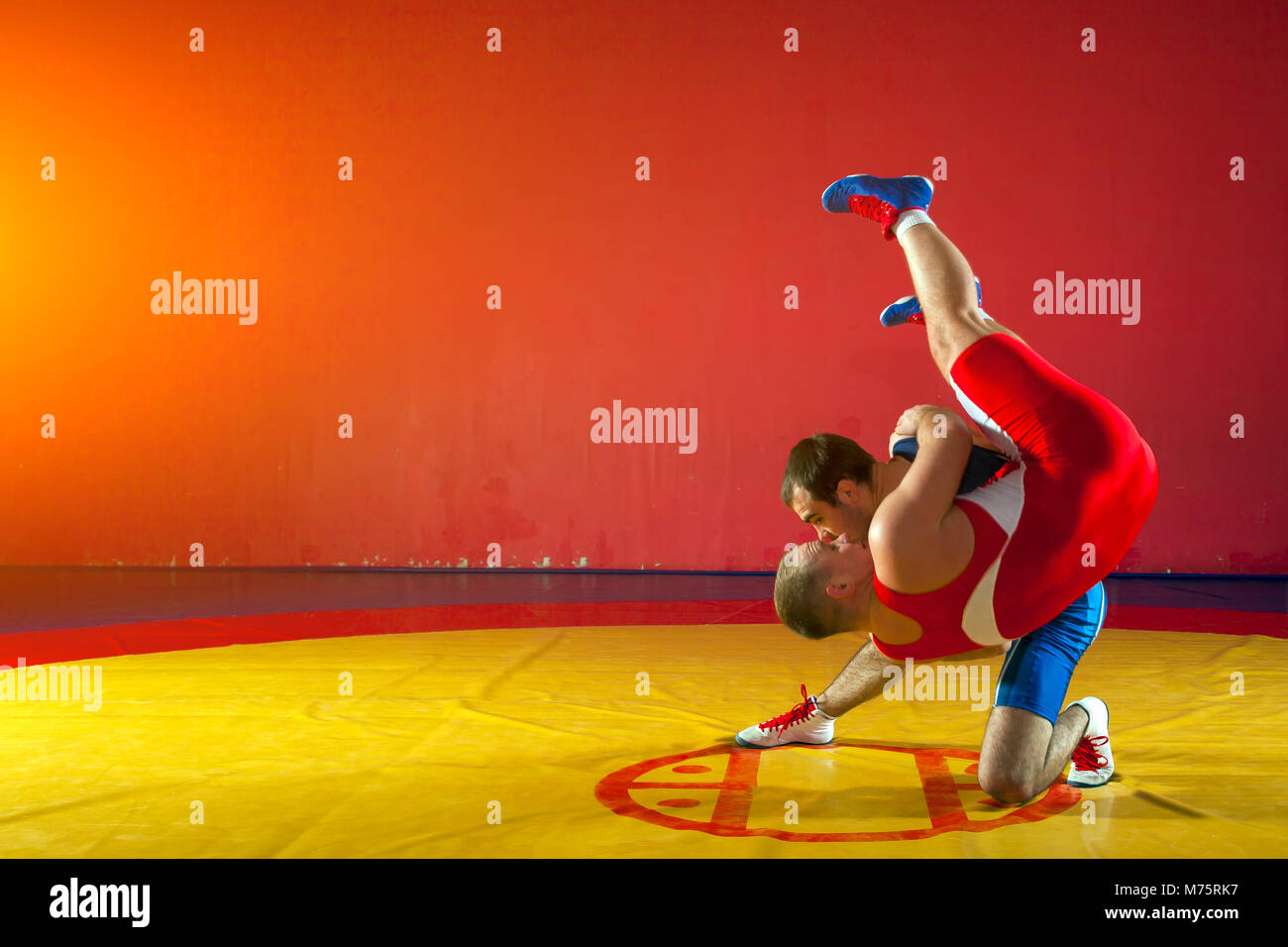 Deux lutteurs forte en bleu et rouge wrestling collants sont wrestlng et faire une suplex wrestling wrestling jaune sur un tapis dans la salle de sport. Jeune homme ne Banque D'Images