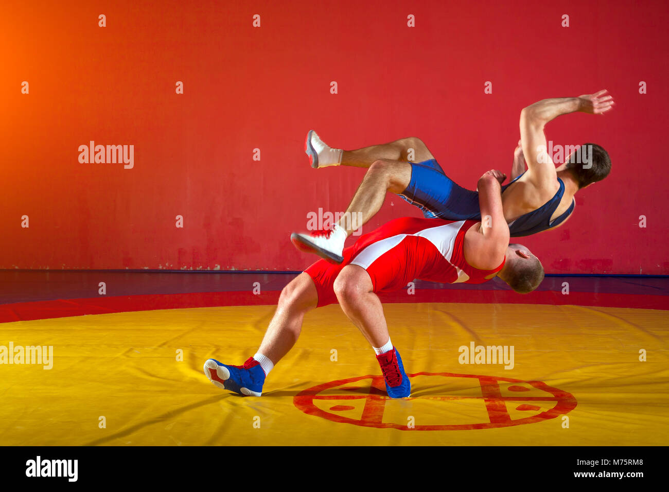 Deux lutteurs gréco-romain en uniforme rouge et bleu sur fond de lutte sur un tapis de lutte jaune dans la salle de sport Banque D'Images
