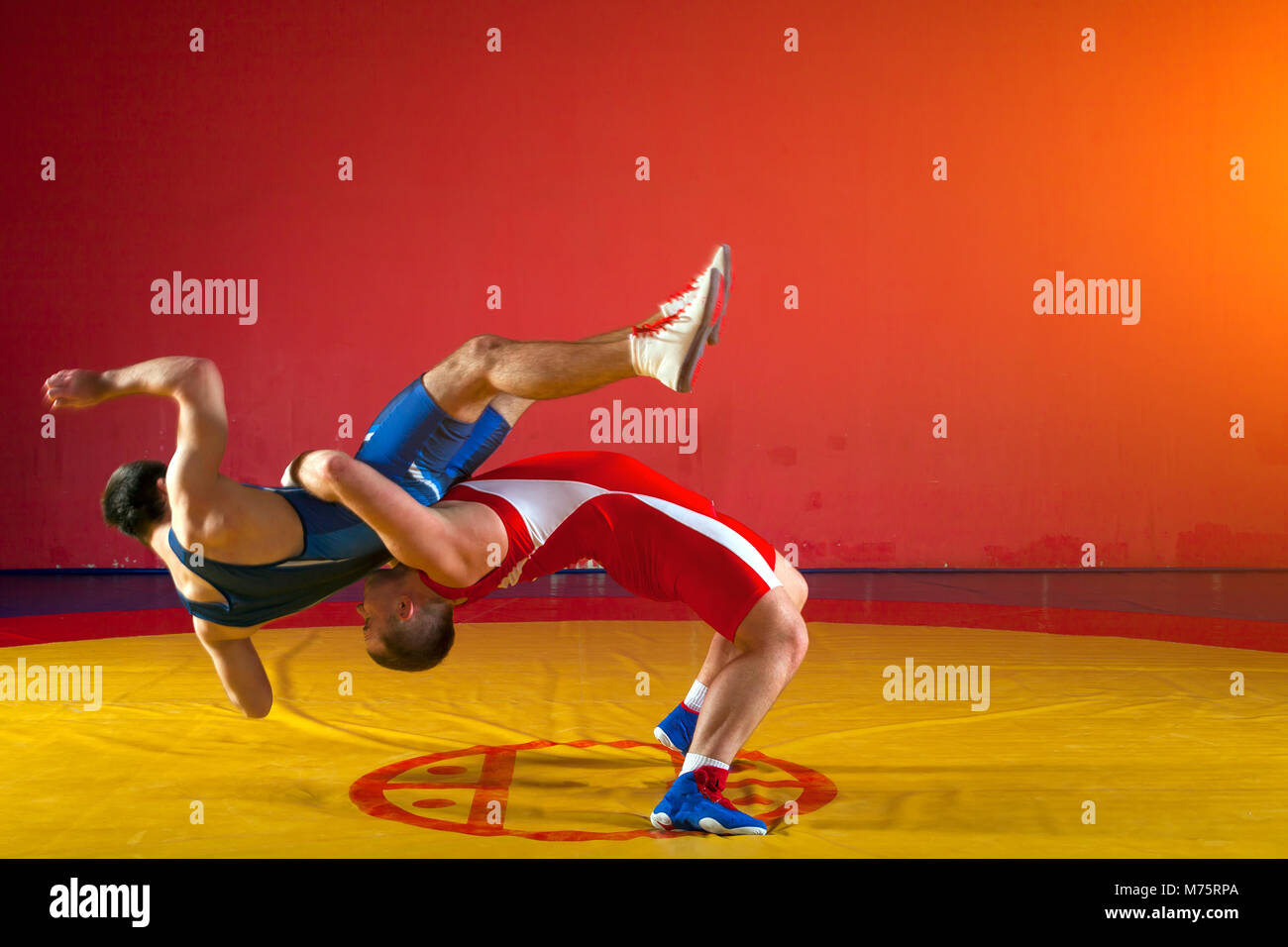 Deux lutteurs gréco-romain en uniforme rouge et bleu sur fond de lutte sur un tapis de lutte jaune dans la salle de sport Banque D'Images