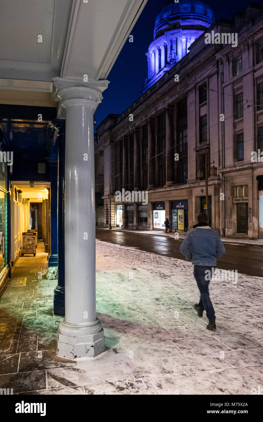 Un homme marche sur une rue de ville de nuit avec de la neige sur le sol pendant l'hiver, Nottingham, England, UK Banque D'Images