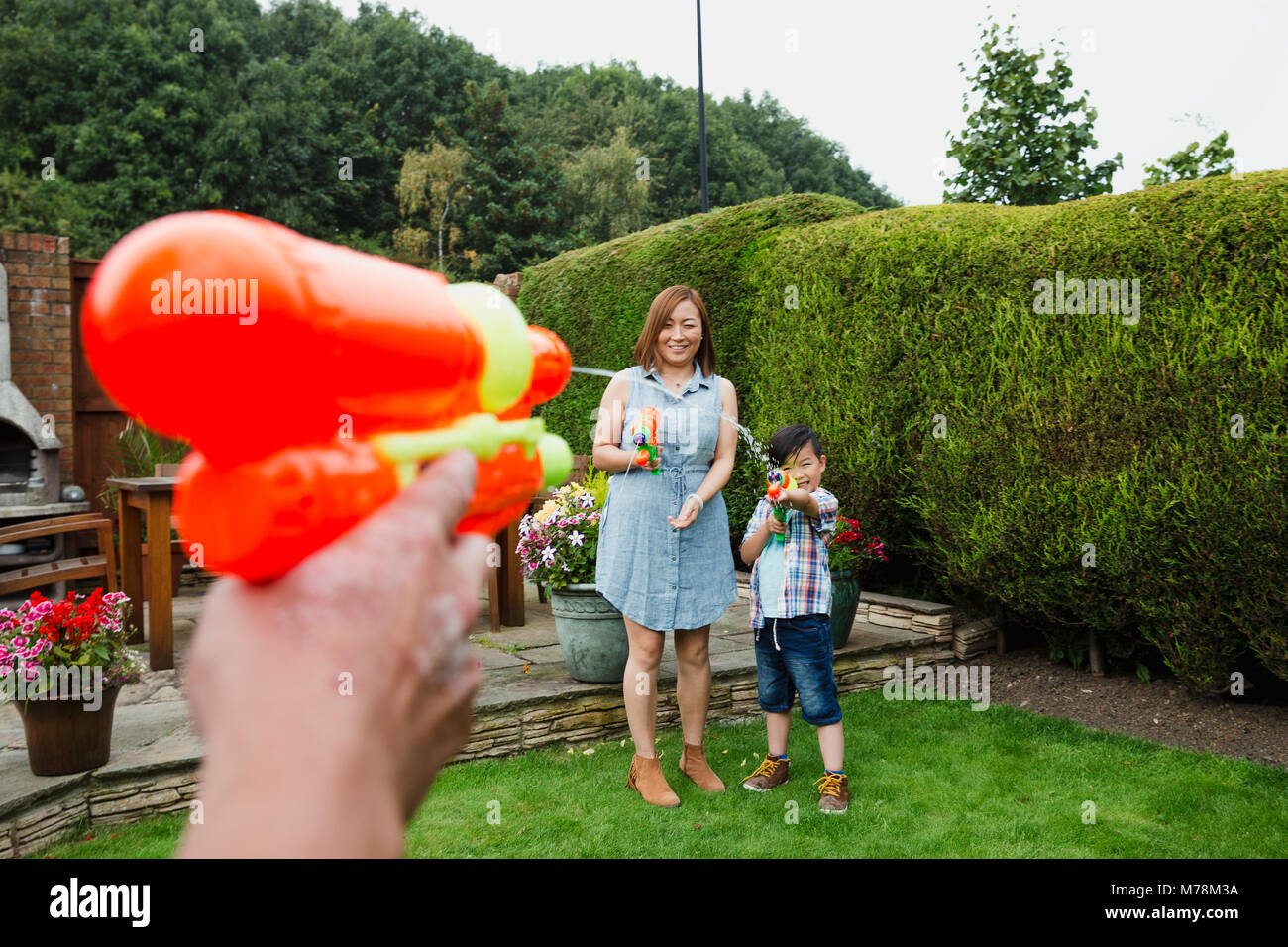 Point de vue d'un homme ayant une lutte de l'eau avec les pistolets à eau dans le jardin avec sa femme et son fils. Banque D'Images