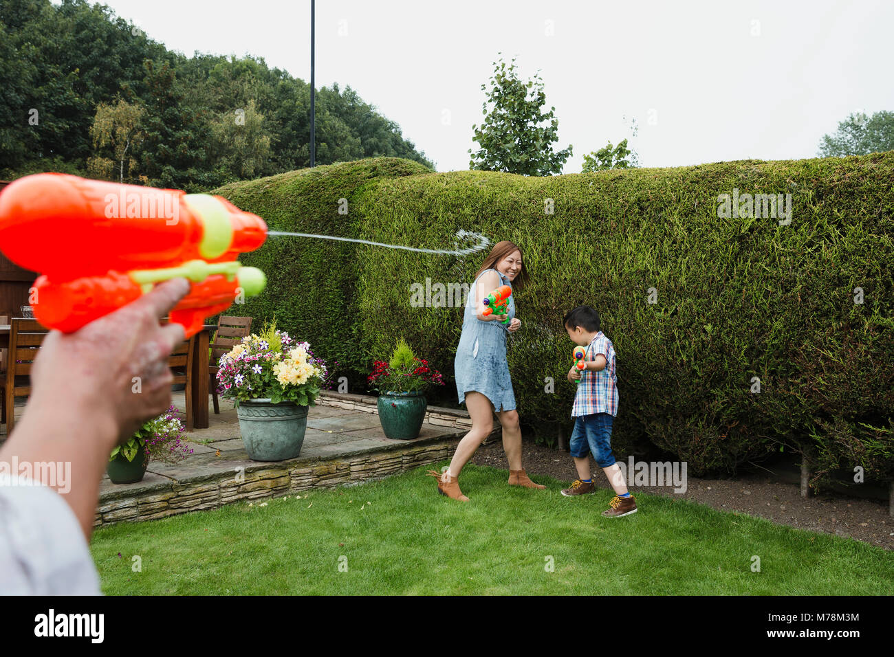 Point de vue d'un homme ayant une lutte de l'eau avec les pistolets à eau dans le jardin avec sa femme et son fils. Banque D'Images