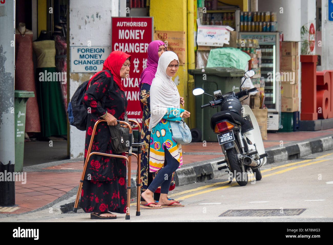 Deux jeunes femmes, et une femme âgée à l'aide d'un dispositif d'aide à la marche, traversant la rue à Singapour. Banque D'Images