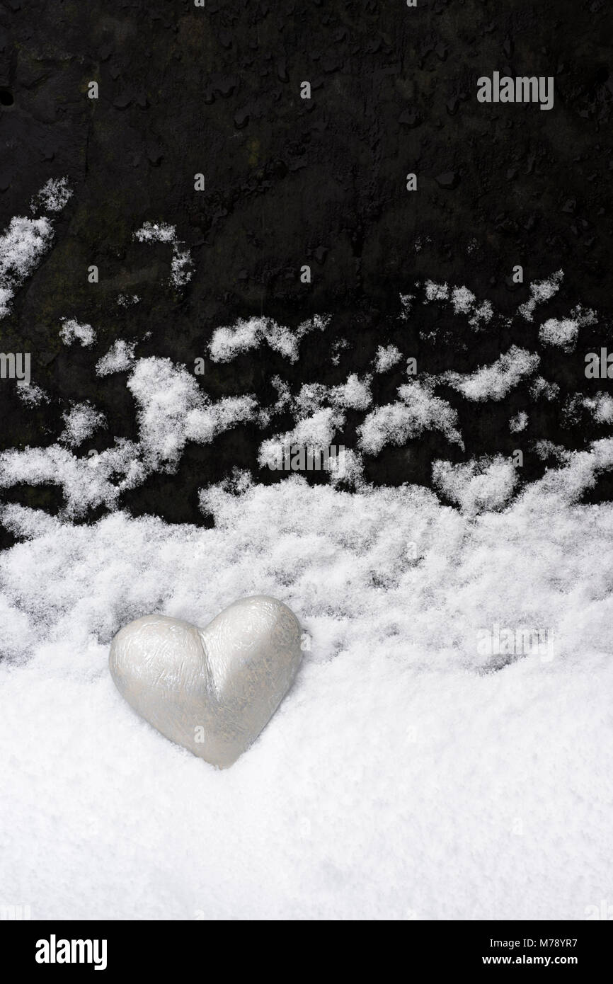 Peint en gris argent coeur placé contre l'ardoise de toiture sur laquelle la neige a réglé. Un paysage en minature imitant la neige qui tombe à travers un ciel sombre Banque D'Images