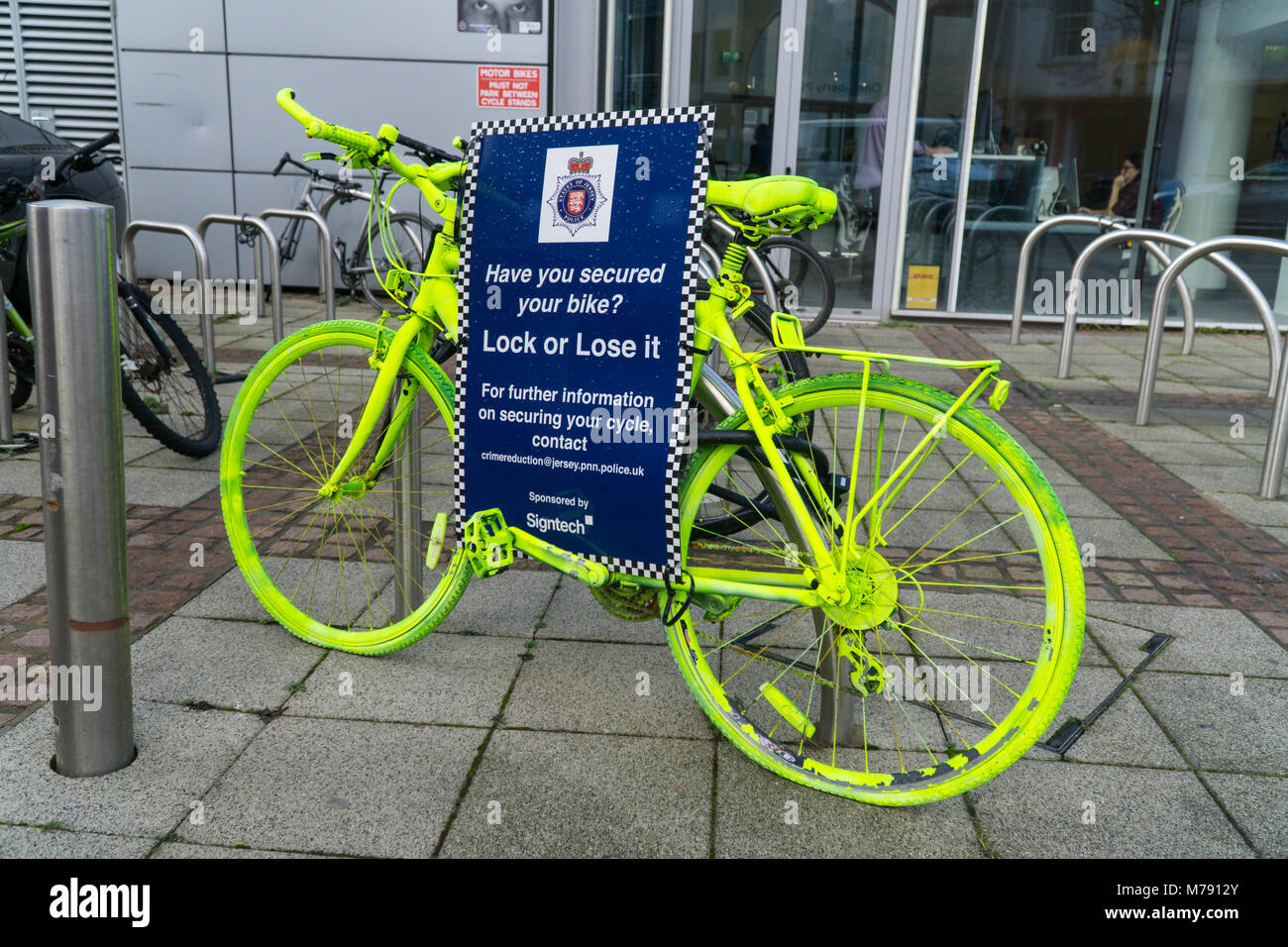 Un vélo vert vif fixé au porte-vélo avec un cadenas comme un message de prévention du crime par la police des États de Jersey, Channel Islands Banque D'Images