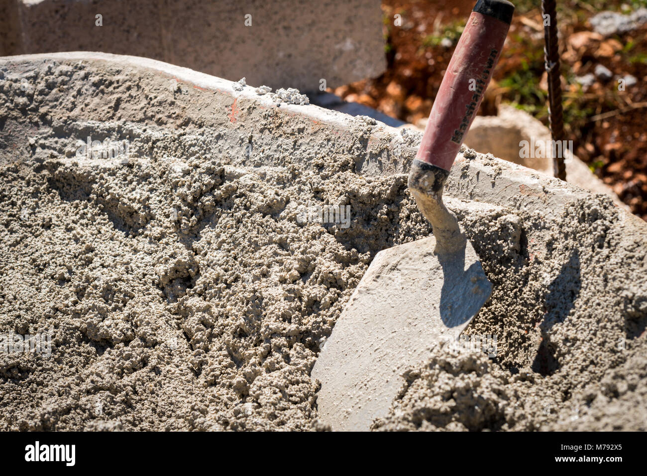 Site de construction avec les travailleurs à l'aide d'une truelle pour répandre le ciment mouillé de brouette sur des blocs de ciment pour construire un mur de béton avec des tiges d'acier Banque D'Images