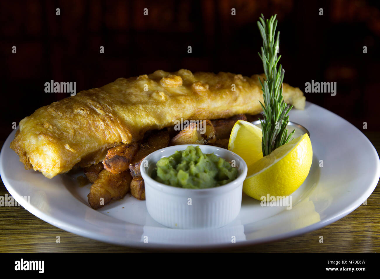 Fish and Chips servis sur une plaque à Sunderland, en Angleterre. Le plat est servi avec un bol de petits pois et d'un morceau de citron. Banque D'Images
