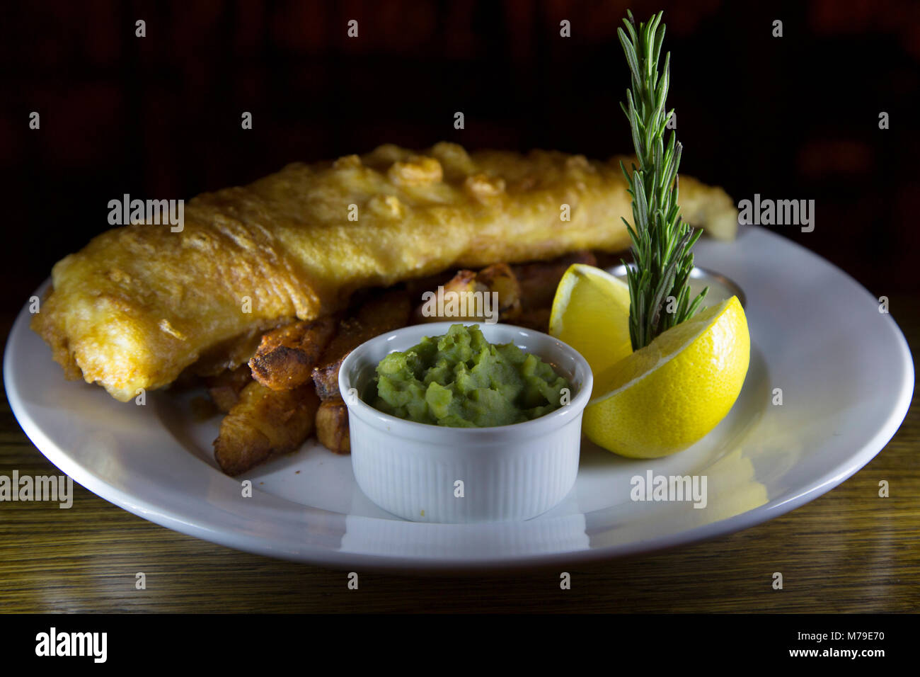 Fish and Chips servis sur une plaque à Sunderland, en Angleterre. Le plat est servi avec un bol de petits pois et d'un morceau de citron. Banque D'Images
