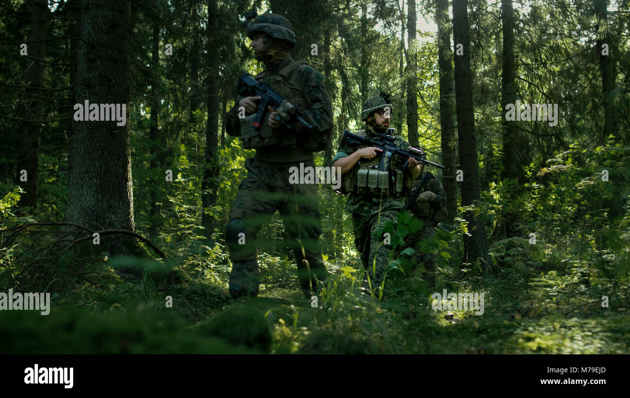 Escouade de cinq soldats entièrement équipés sur une reconnaissance de la mission militaire. Ils se déplacent en formation dans une forêt dense. Banque D'Images