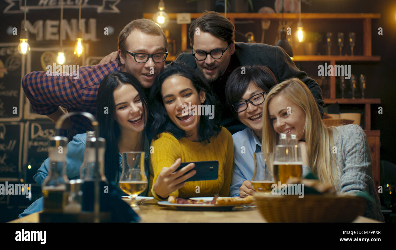 Au bar/ restaurant Hispanic Woman prend des Selfies elle-même et ses meilleurs amis. Beau groupe de jeunes en établissement élégant. Banque D'Images