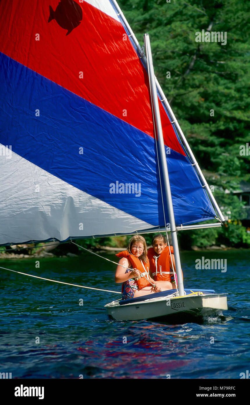 Deux jeunes filles voile un bateau conseil sur un lac au camp d'été à New York, United States, Amérique du Nord. Banque D'Images