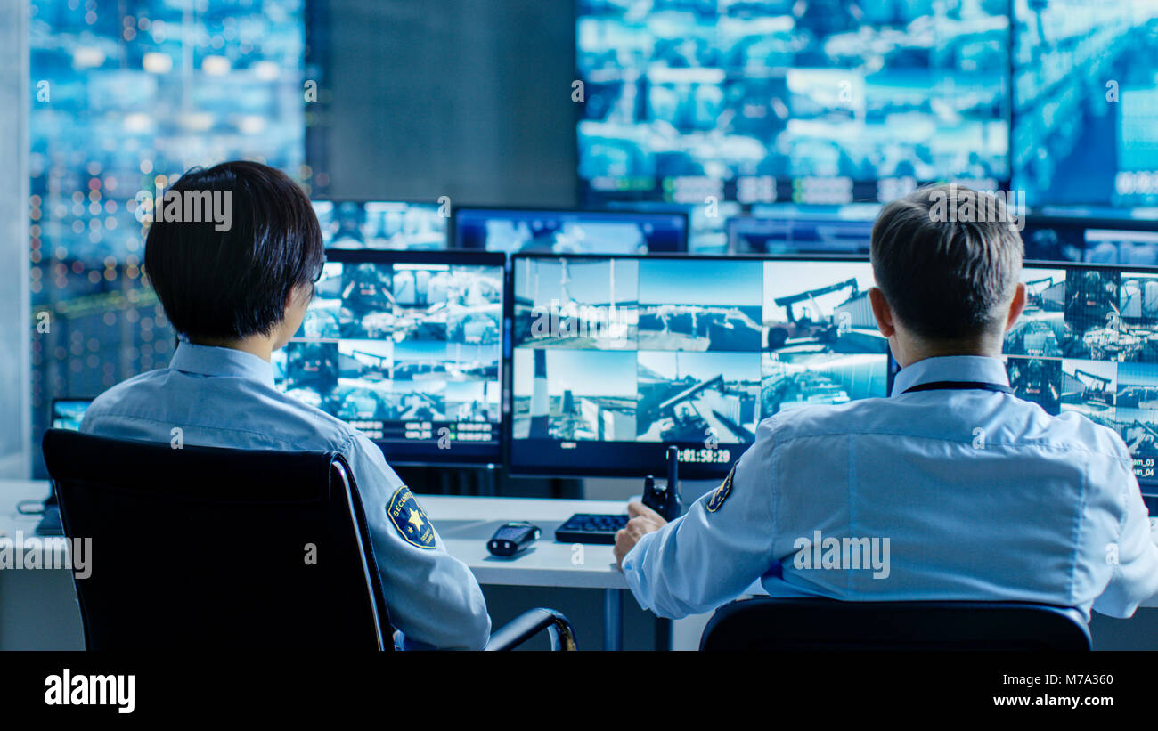 Dans la salle de contrôle de la sécurité Deux agents surveiller plusieurs écrans pour les activités suspectes, ils signalent toute activité non autorisée. Banque D'Images