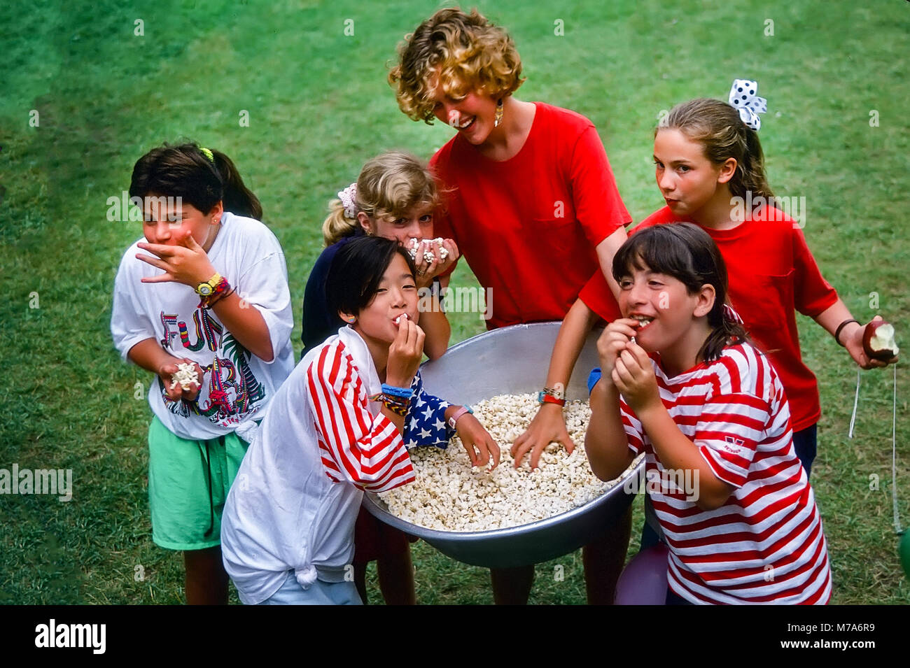 Happy girl les enfants mangent du popcorn à partir d'un grand bassin avec leur conseiller à un camp d'été filles dans le Vermont, USA Banque D'Images