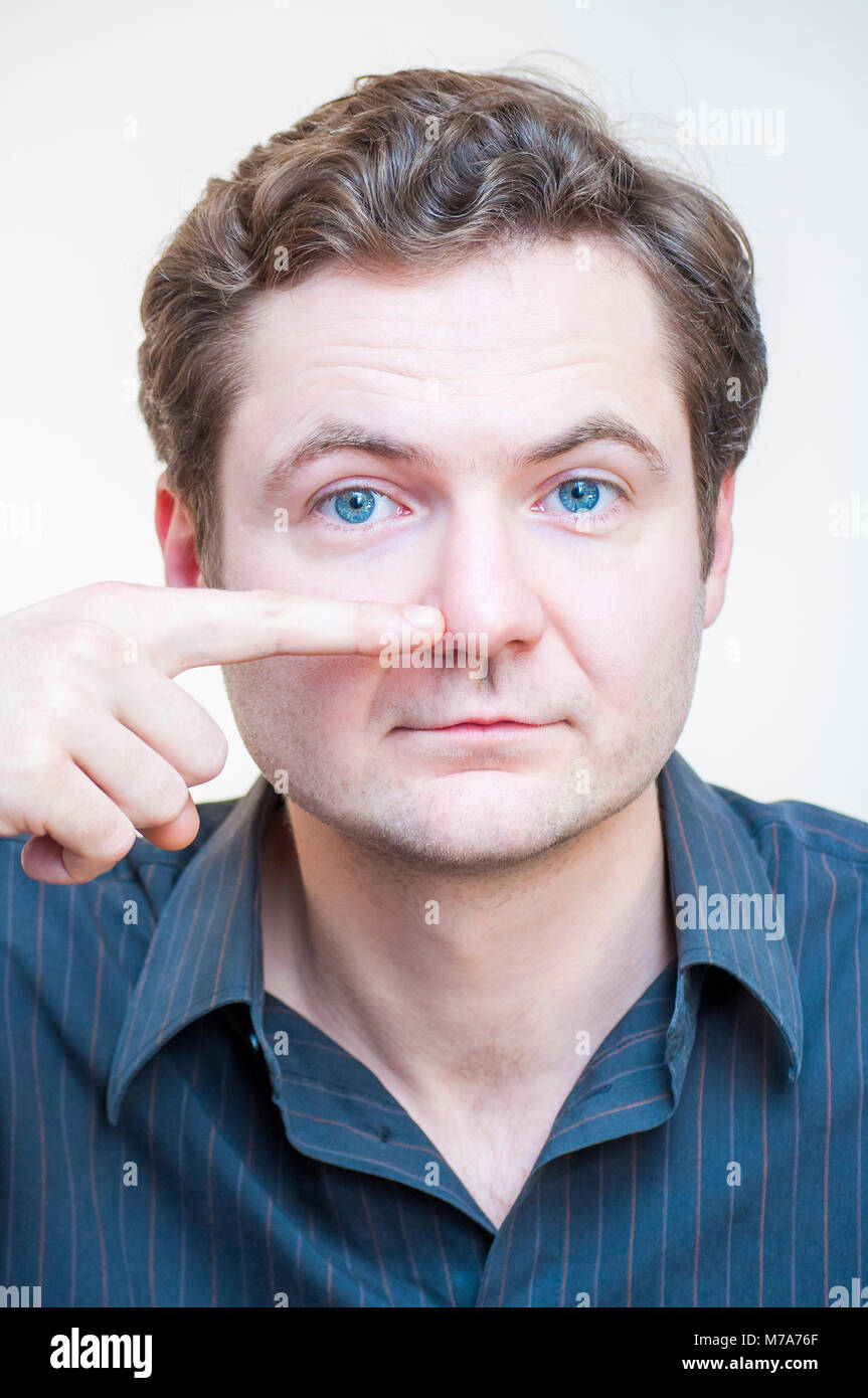 Portrait of young Caucasian ethnicité blue-eyed man points sur son nez sur fond blanc. Pièces à visage humain. Banque D'Images