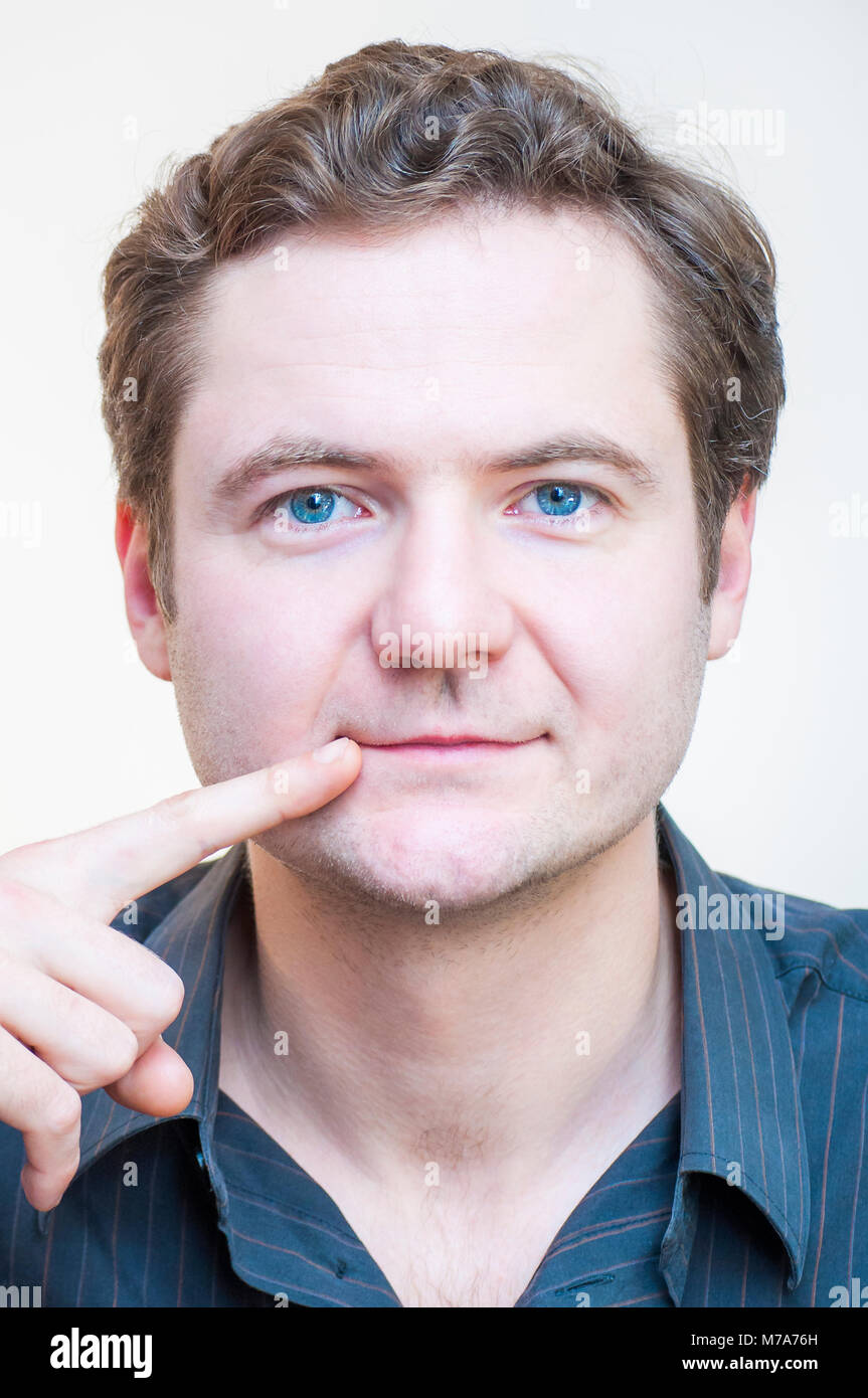 Portrait of young Caucasian ethnicité blue-eyed man points sur ses lèvres sur fond blanc. Pièces à visage humain. Banque D'Images