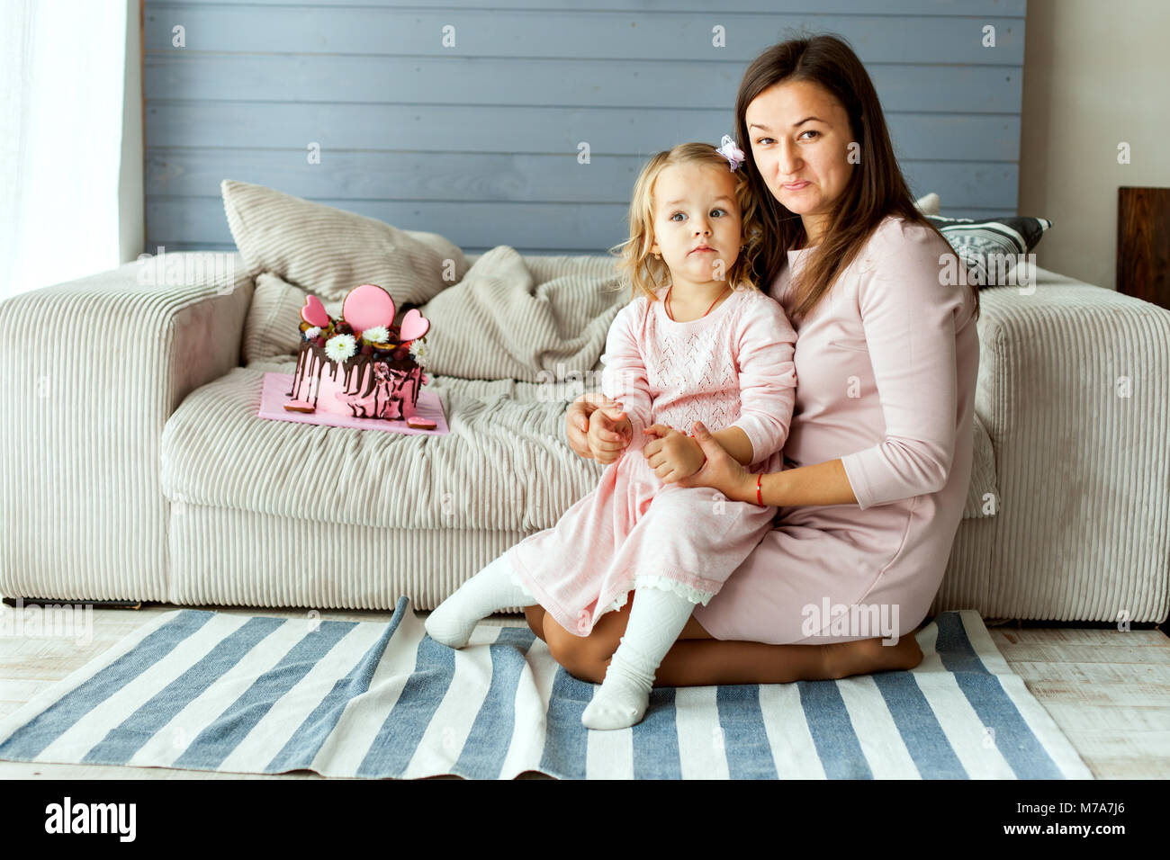 Fille avec sa mère assise à côté de la table. Il y a un gâteau d'anniversaire sur la table Banque D'Images