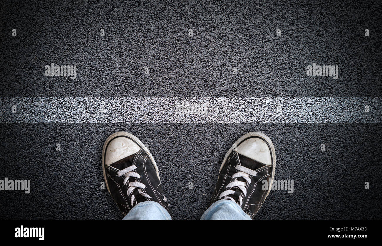 Un adolescent en jeans et chaussures de toile debout sur la route d'asphalte derrière une ligne avec copie espace. Concept de debout à une ligne de départ, un nouveau départ, Banque D'Images