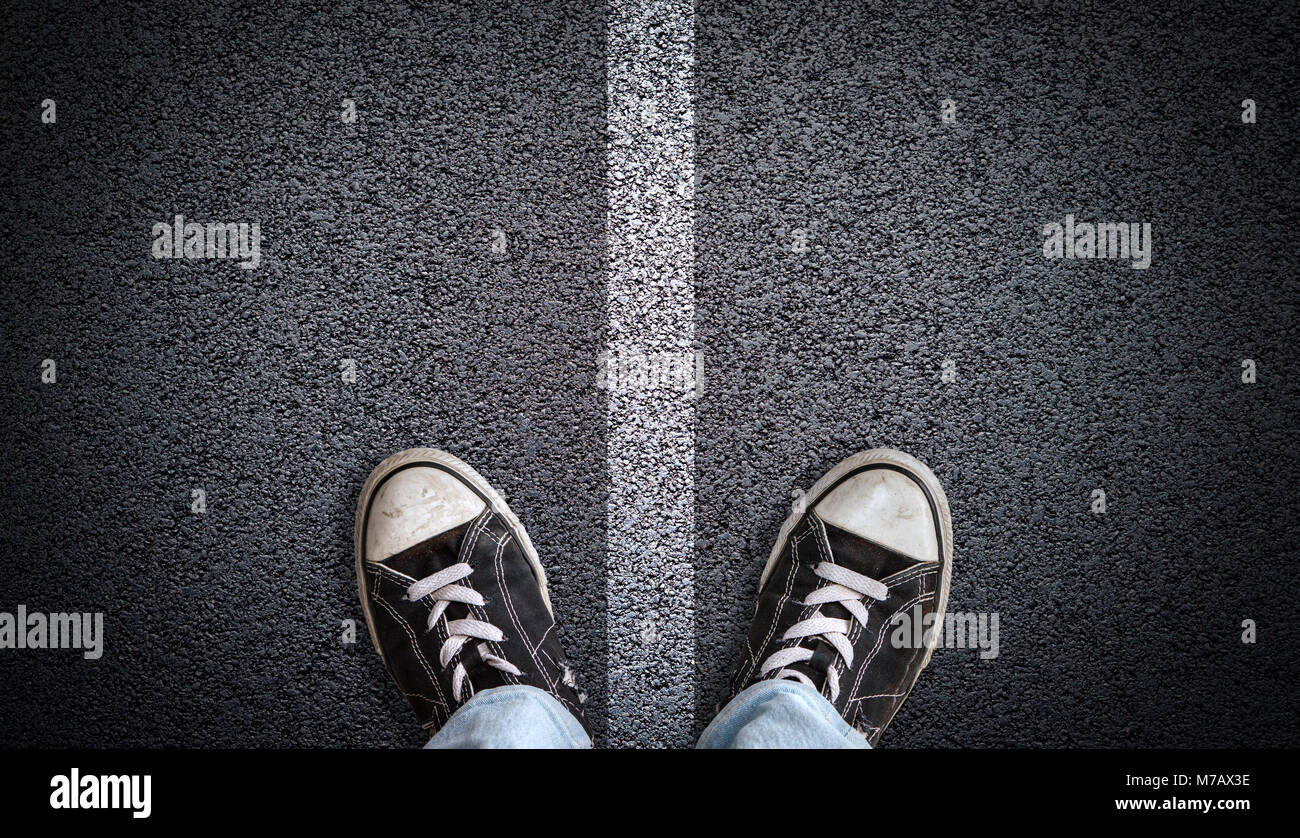 Un adolescent en jeans et chaussures de toile debout sur la route d'asphalte de la route avec marquage du diviseur dans le centre et l'espace de copie. Concept de l'article sur la croix Banque D'Images