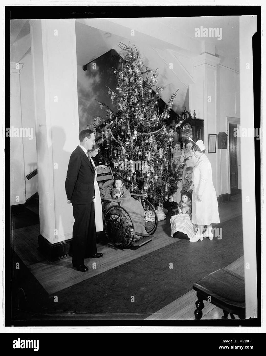 Une scène de vacances montrant des enfants en fauteuil roulant rassemblés autour d'un arbre de Noël, soulignant l'inclusivité et la célébration. Banque D'Images