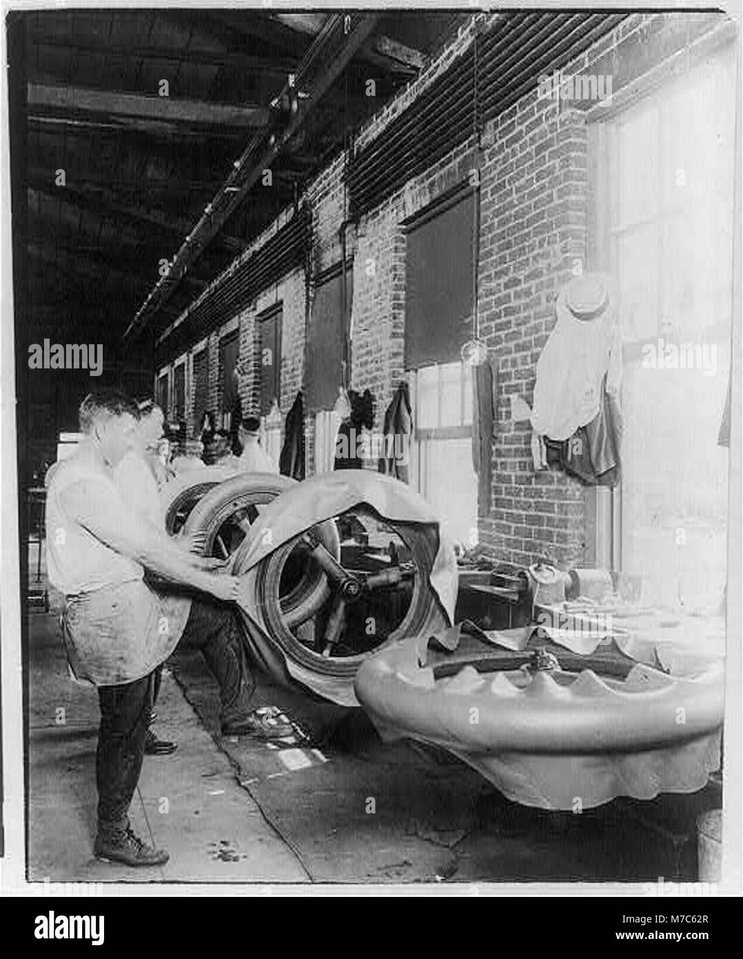 Une photographie documentant le processus de fabrication de pneus faits à la main, montrant le travailleur pendant qu'il applique le premier pli. Cette image met en évidence un processus industriel précoce dans la fabrication de pneus. Banque D'Images