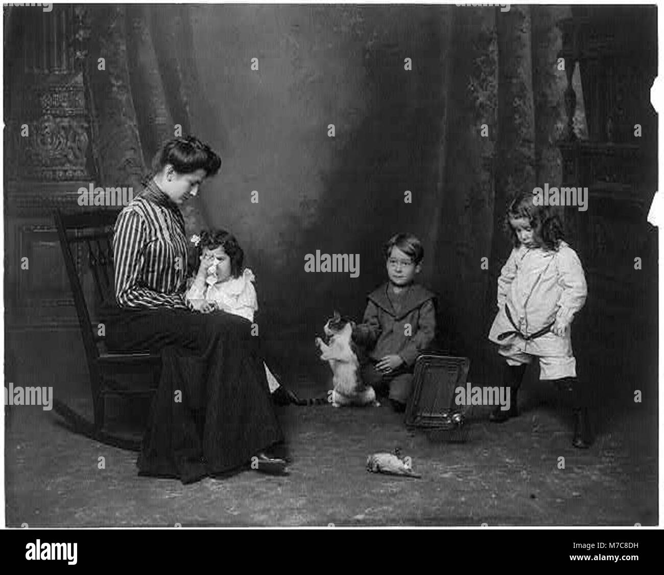 Cette photographie émouvante montre une femme et deux filles pleurant un oiseau mort, tandis qu'un garçon tient un chat, capturant un moment poignant d'interaction homme-animal. Banque D'Images