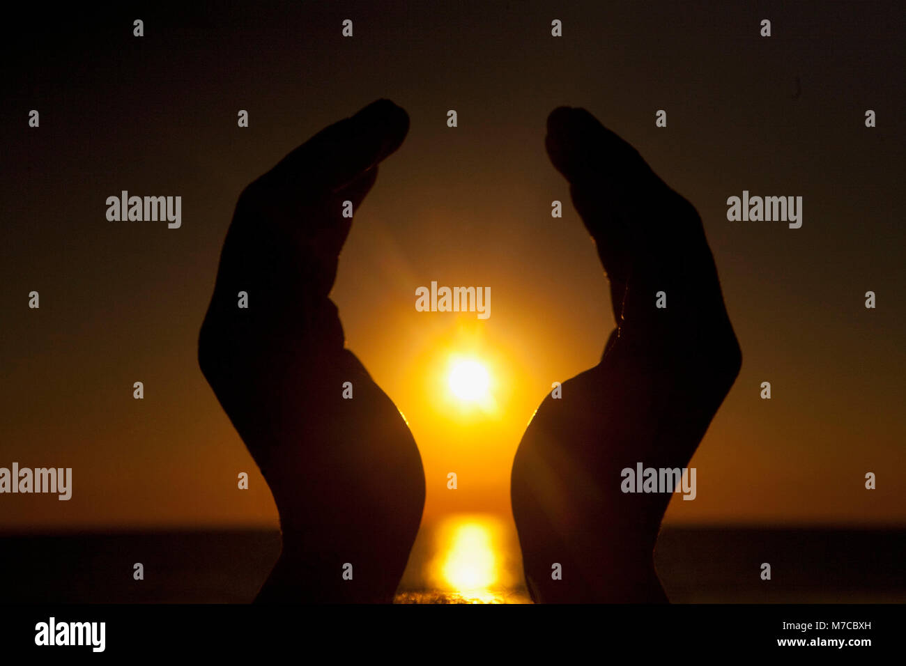 Les mains feignant de tenir le soleil couchant, Miami Beach, Florida, USA Banque D'Images