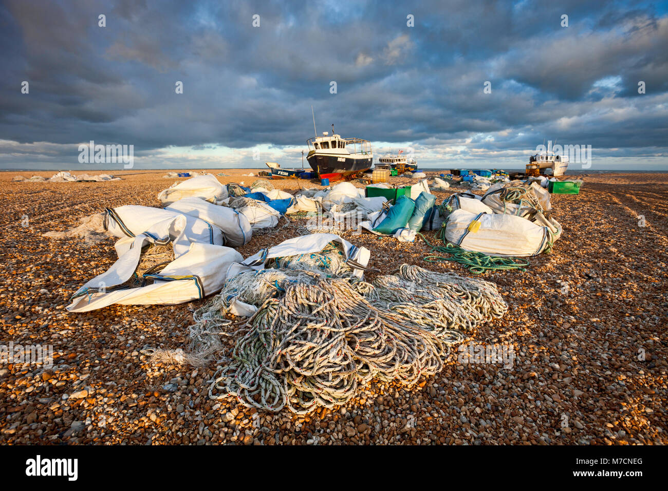 Les bateaux de pêche et des filets sur la plage de galets à Dungeness, Kent, UK au cours de belle lumière et sous un ciel dramatique. Banque D'Images