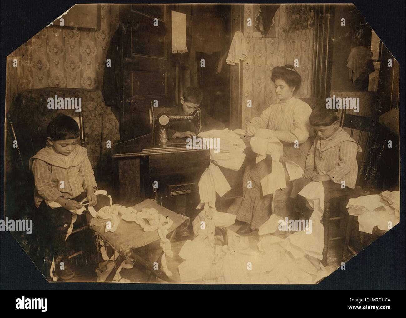 Une photographie représentant des enfants de la famille Romana fabriquant des robes pour Campbell Kid Dolls dans une salle de logement au 4e étage du 59 Thompson Street, New York. L'image montre le travail des enfants dans de mauvaises conditions. Banque D'Images