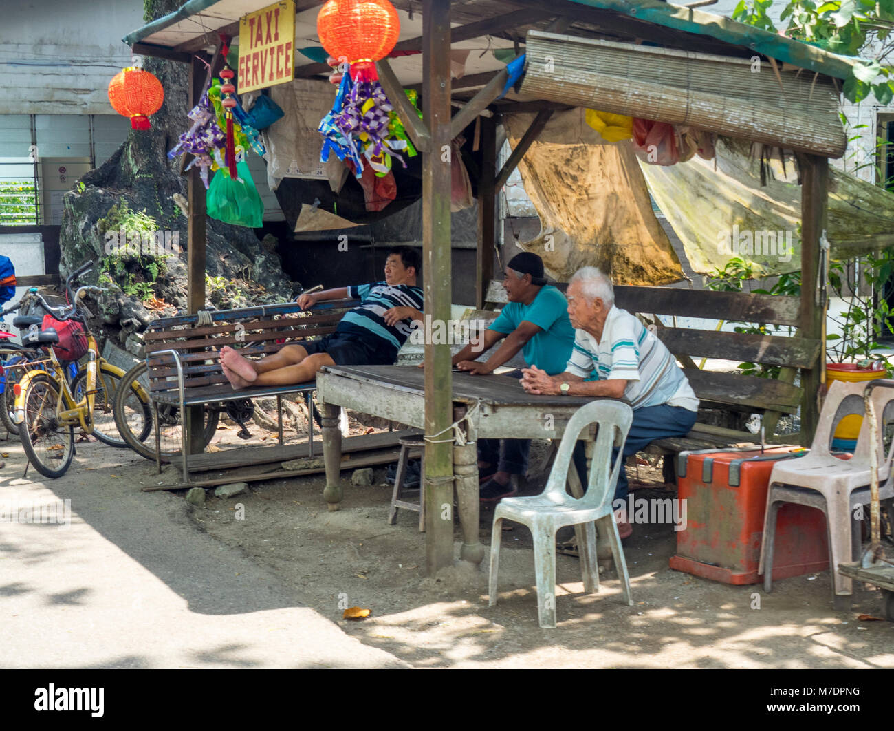 Trois personnes âgées les chauffeurs de taxi locaux assis sous un abri en attente de clients de l'île de Pulau Ubin, Singapour. Banque D'Images