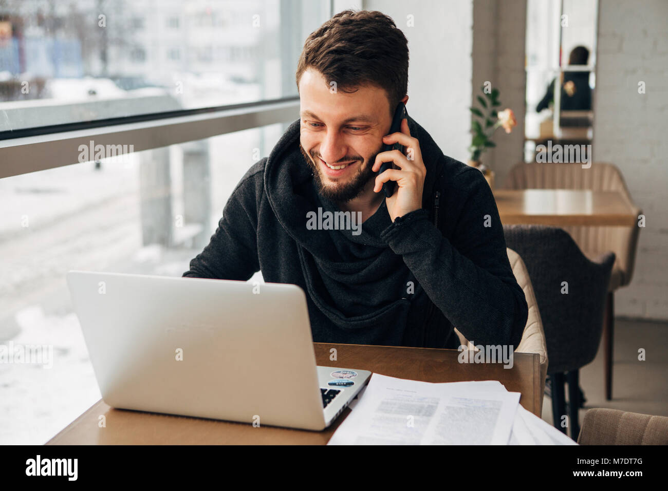 Un jeune homme parler au téléphone et de travailler à un ordinateur portable dans un café Banque D'Images