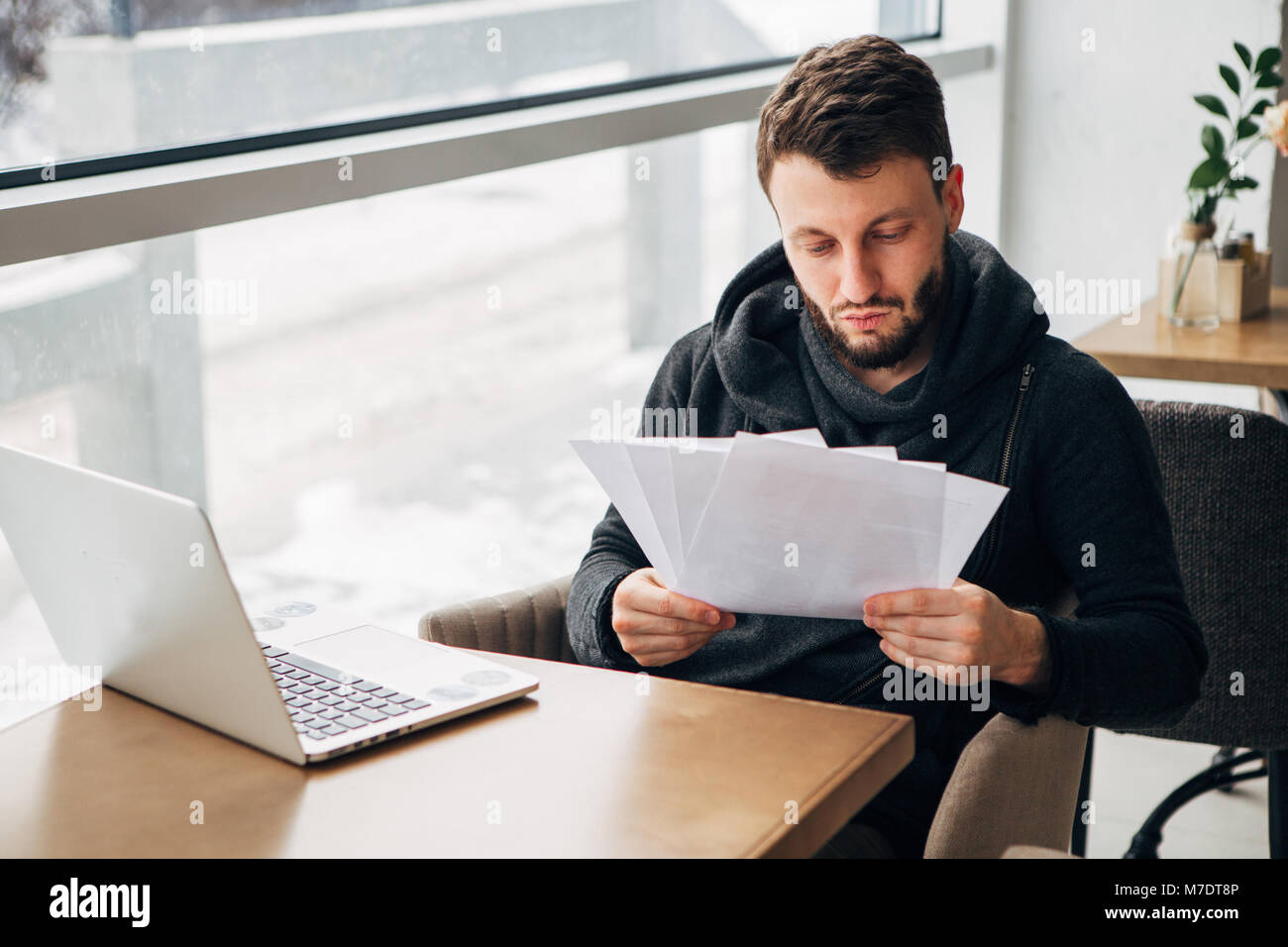 Jeune homme barbu concentré Tshirt vêtu de noir pour ordinateur portable de travail Urban Cafe Banque D'Images