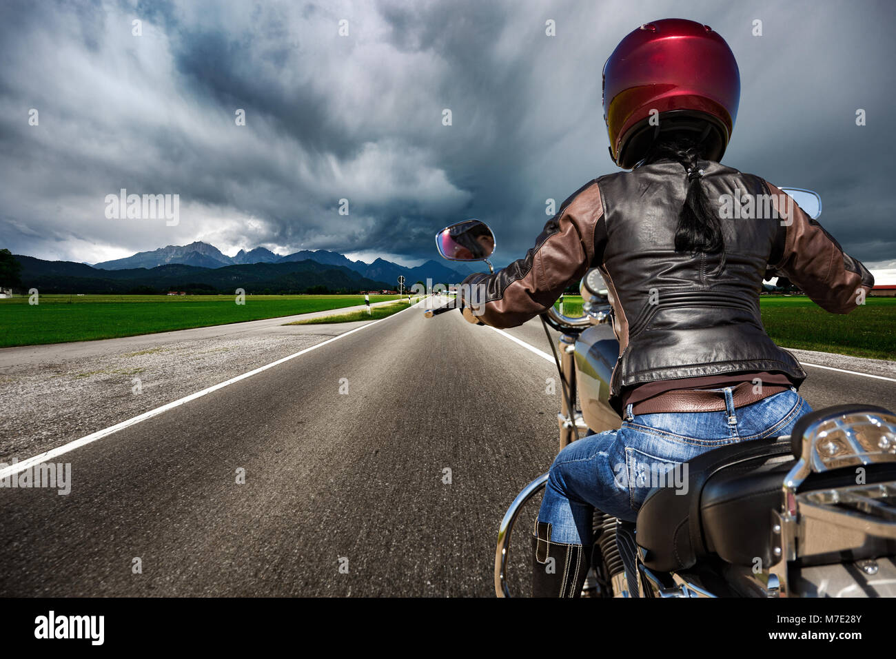 Biker Girl on a motorcycle dévaler la route dans un orage - Forggensee et Schwangau, Bavière, Allemagne Banque D'Images