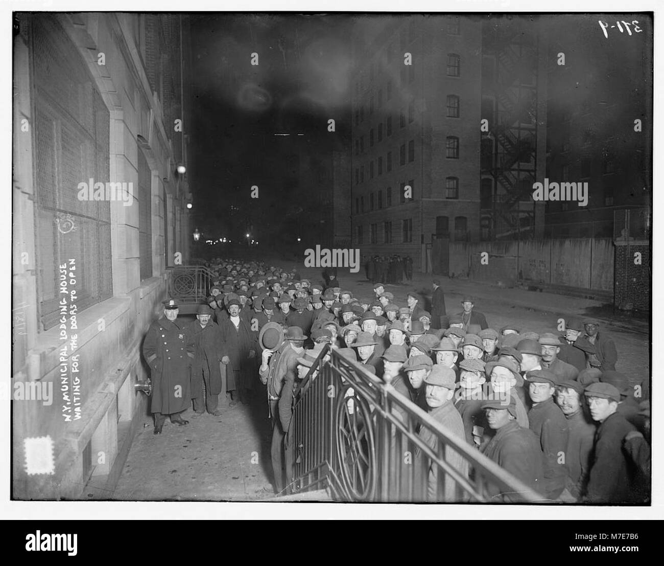 Une photographie montrant des individus attendant devant la maison municipale de New York, soulignant le rôle du bâtiment dans l'hébergement temporaire des sans-abri au début du XXe siècle. Banque D'Images