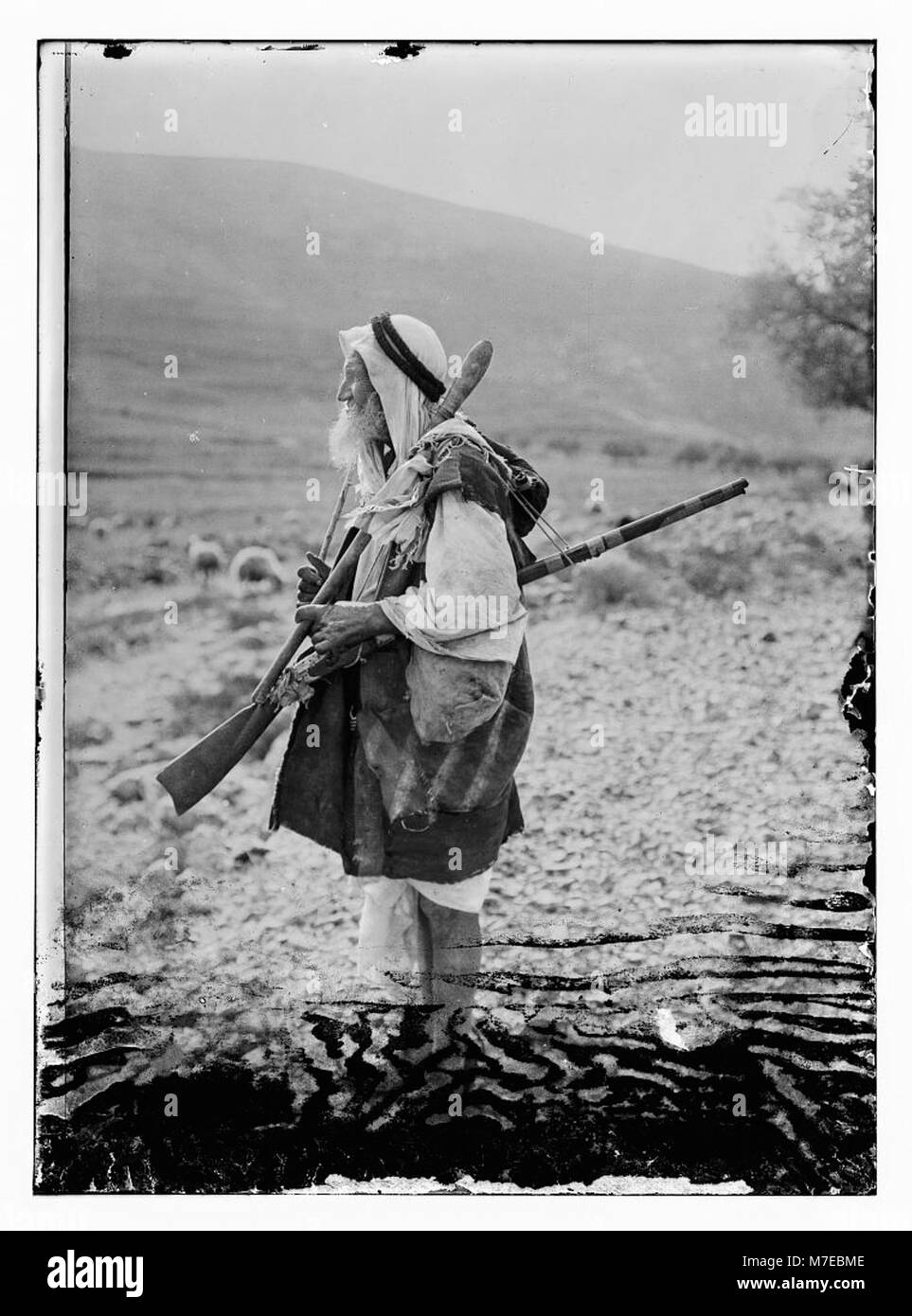 Cette image représente un berger âgé de Gibeon, une région historique mentionnée dans les textes bibliques. Il est vu avec sa canne, son bâton et un fusil à dos de silex, représentant des outils de berger traditionnels utilisés dans les temps anciens. Banque D'Images