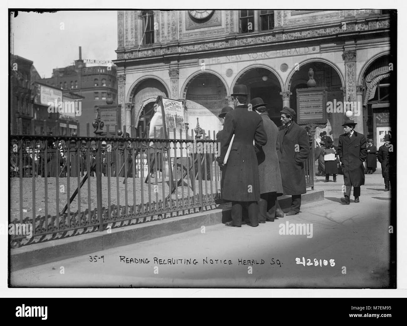 Une photographie historique montrant des individus lisant une publicité de recrutement à Herald Square, New York, soulignant l'engagement du public dans la propagande en temps de guerre. Banque D'Images