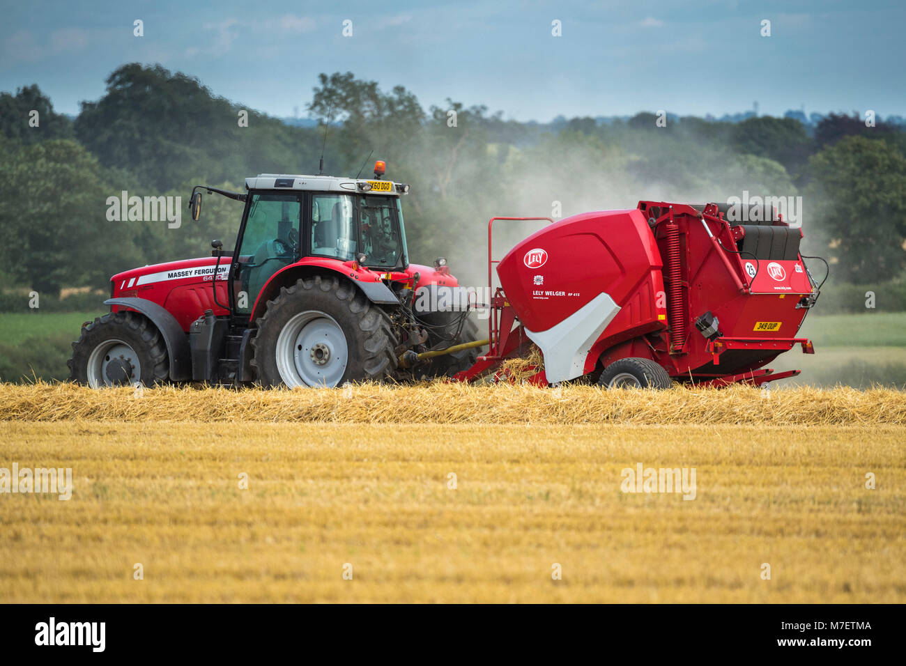 Agriculteur ou l'homme en rouge lumineux tracteur agricole tirant une ramasseuse-presse, est conduite et travaillant dans un champ, le pressage de paille - Whixley, North Yorkshire, Angleterre, Royaume-Uni. Banque D'Images