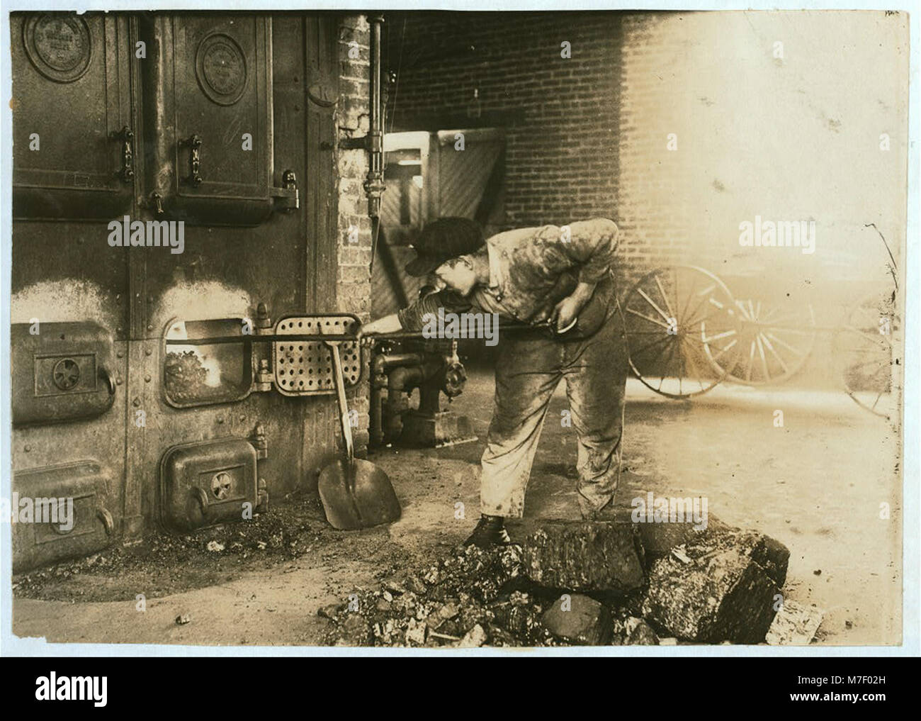 Une photographie montrant un garçon alimentant la fournaise dans la centrale électrique de l'école de formation Pauls Valley, soulignant sa fierté pour son travail et l'environnement industriel. Banque D'Images
