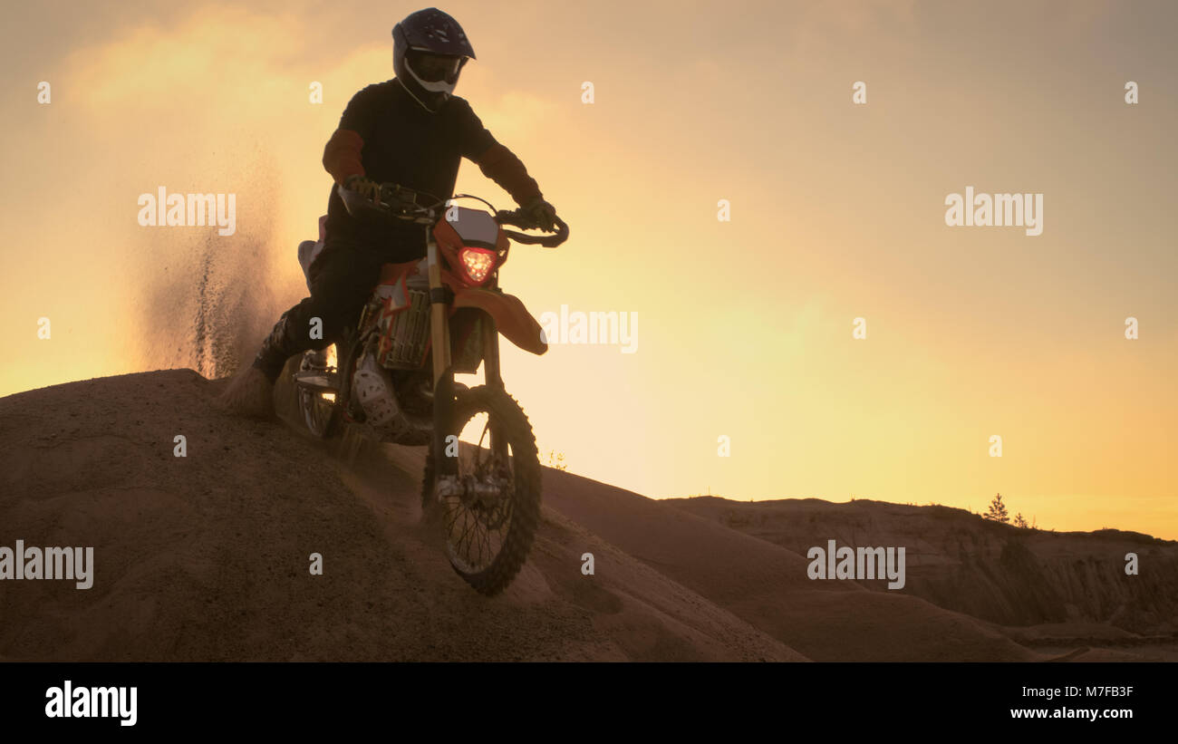 Pilote Moto Motocross professionnels durs sur la dune et s'arrête sur le haut. C'est l'heure du coucher du soleil et la voie est recouverte de brouillard de fumée/. Banque D'Images