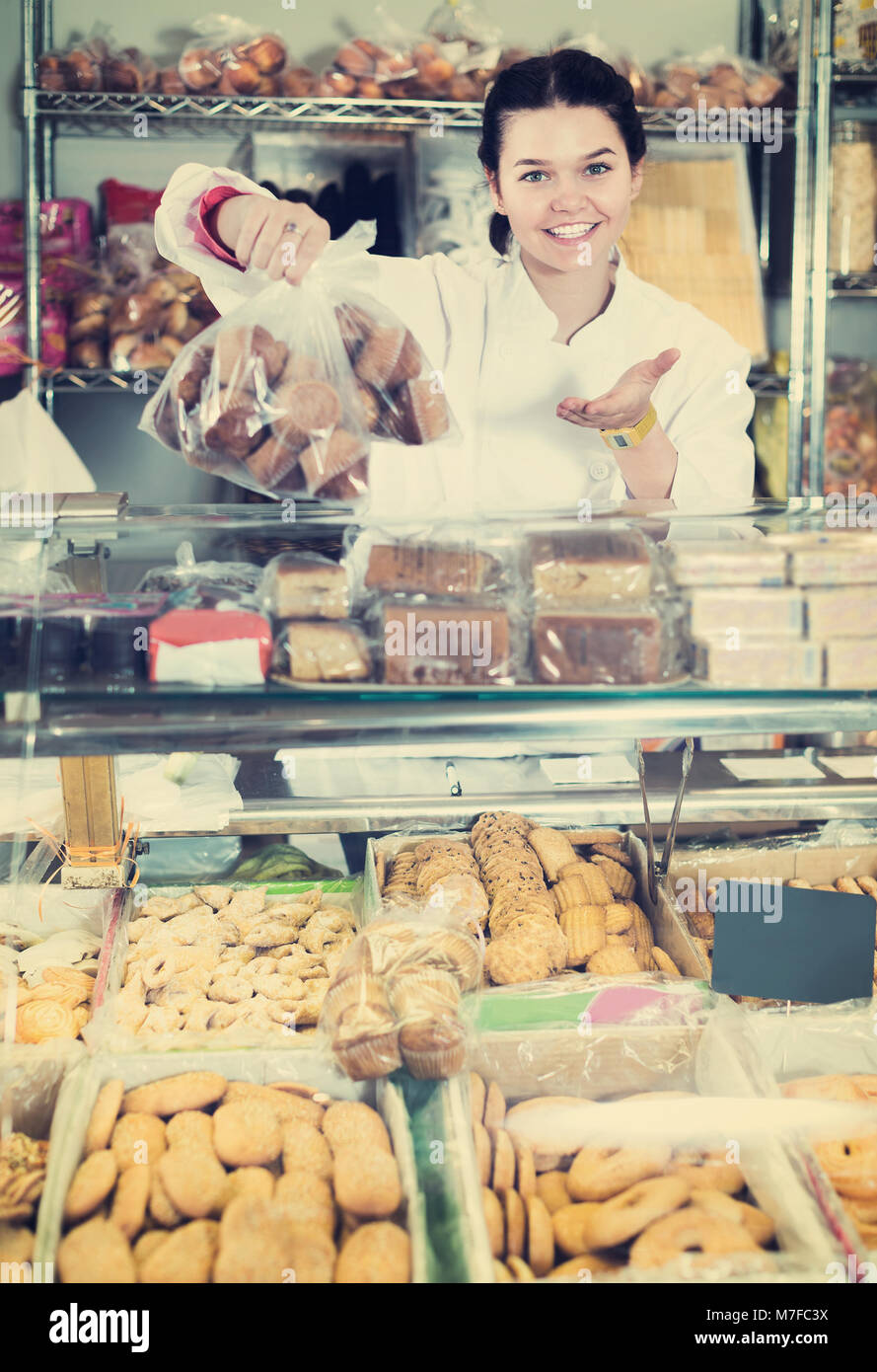 Young smiling saleswoman posant avec cookies au compteur dans sweets shop Banque D'Images
