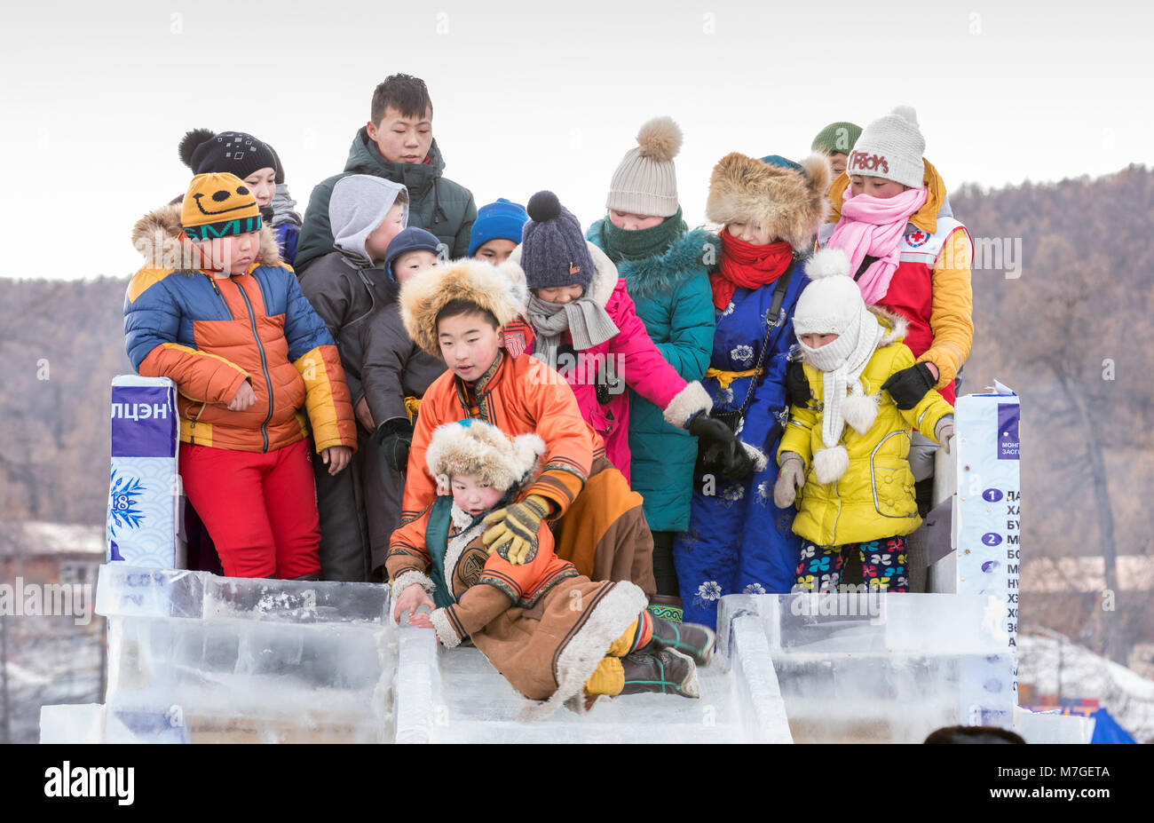 Hatgal, la Mongolie, le 4 mars 2018 : les enfants mongols habillés en vêtements traditionnels sur la glace d'un lac Khuvsgul, descendant un toboggan de glace madeout Banque D'Images