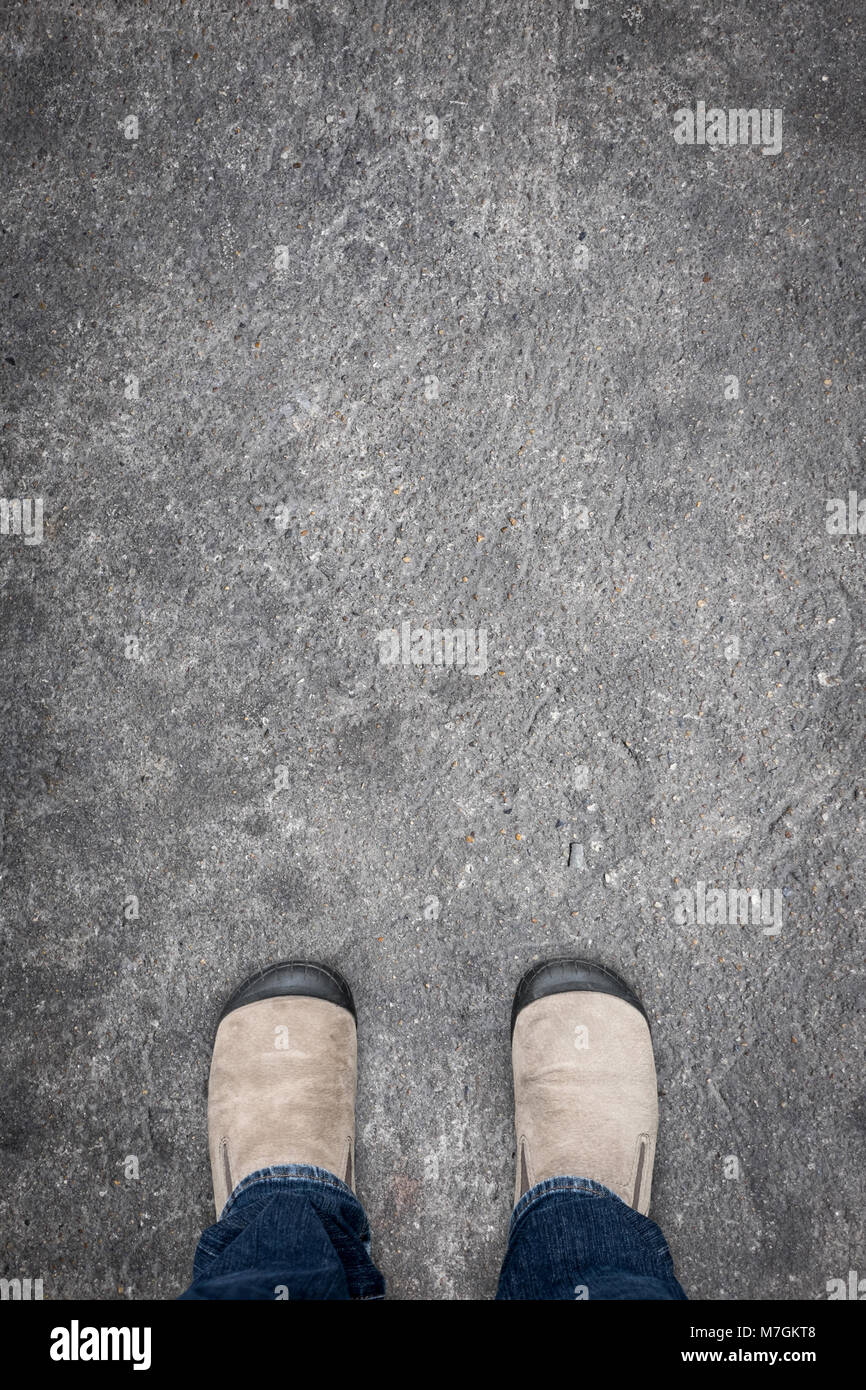 Chaussures en daim marron et bleu jeans debout sur un sol en béton de décider quoi faire ensuite Banque D'Images