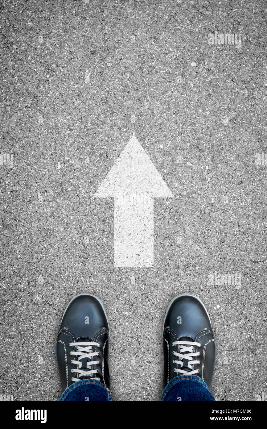 Les chaussures noir debout sur la route de béton bitumineux et blanc direction de dire à aller tout droit. Banque D'Images