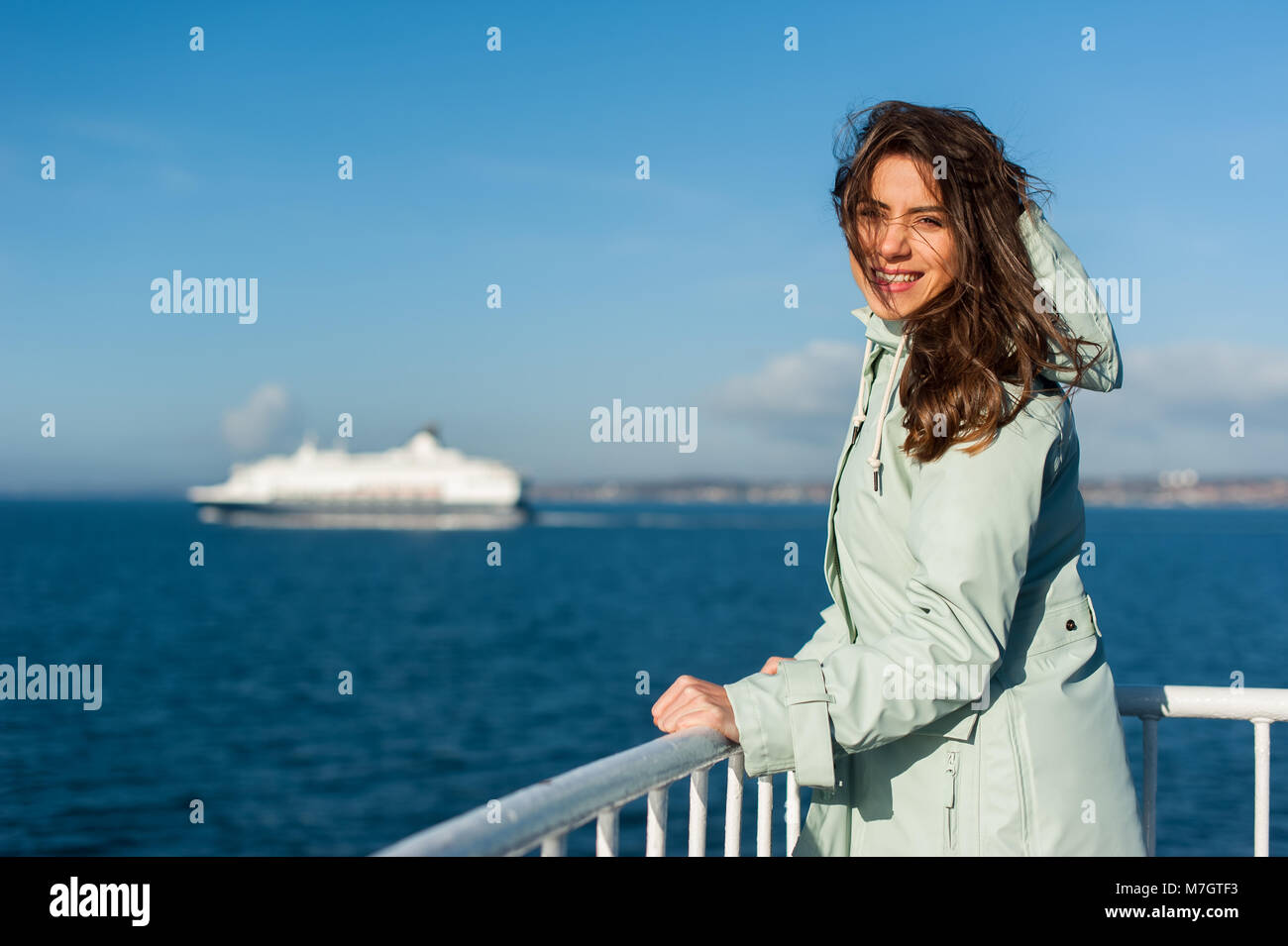 Jeune voyageur femme à la mer, de la voile d'un bateau avec gros bateau de croisière ou en ferry sur l'arrière-plan, portant une veste de pluie. Banque D'Images