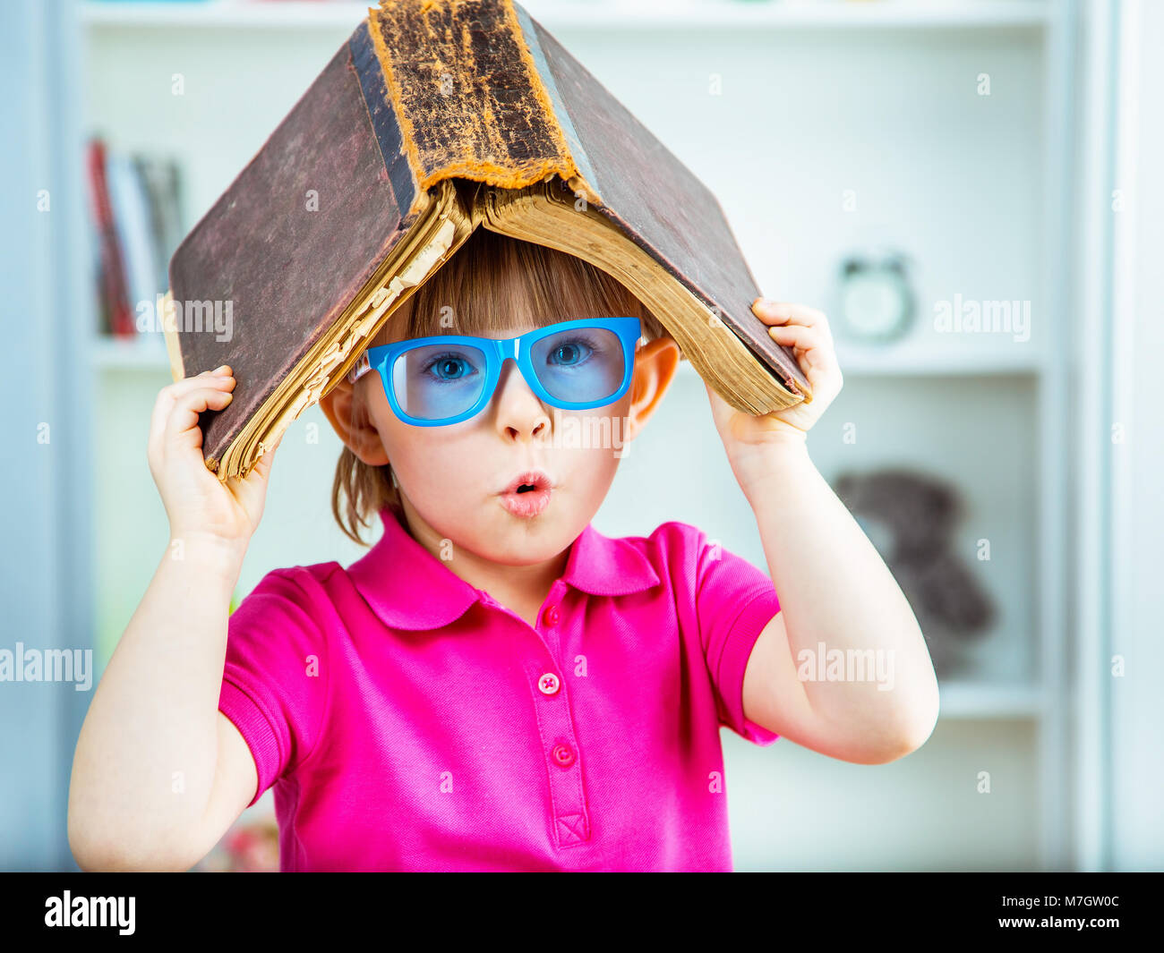 Petite fille avec un vieux livre sur la tête. Banque D'Images