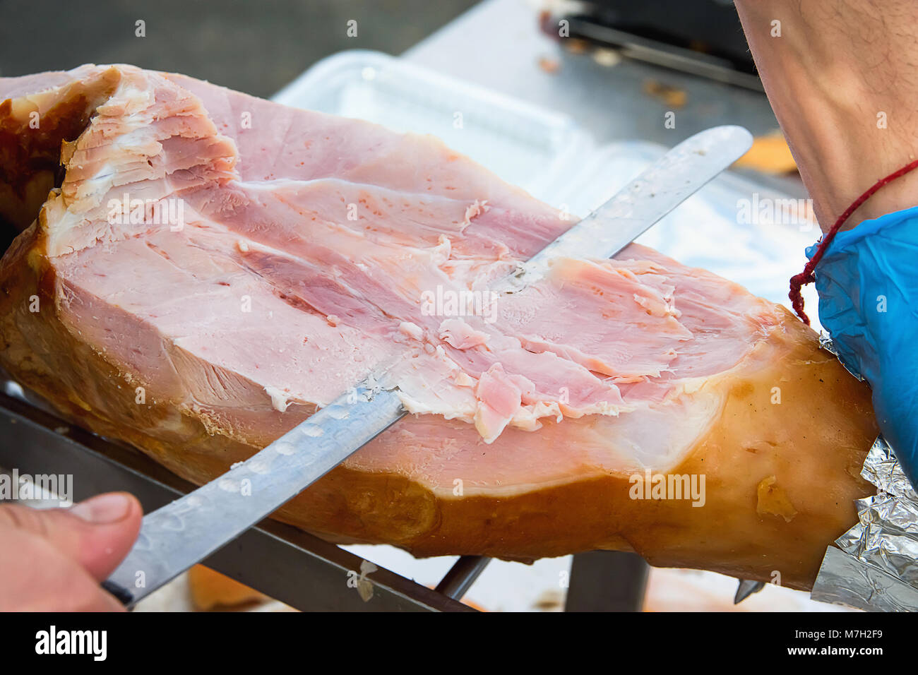 Découpage des agriculteurs avec Long Couteau jambon de porc cuit fumé à partir de la jambe à marché. Close up de texture de la viande. Les couleurs sont éclatantes. Produits biologiques. Style de voyage. Banque D'Images