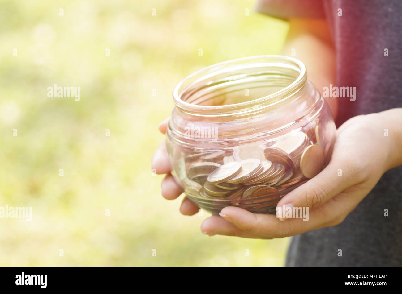 Jeune fille tenir le flacon en verre de pièces pour économiser de l'argent et concept de don dans blur green gardent Banque D'Images