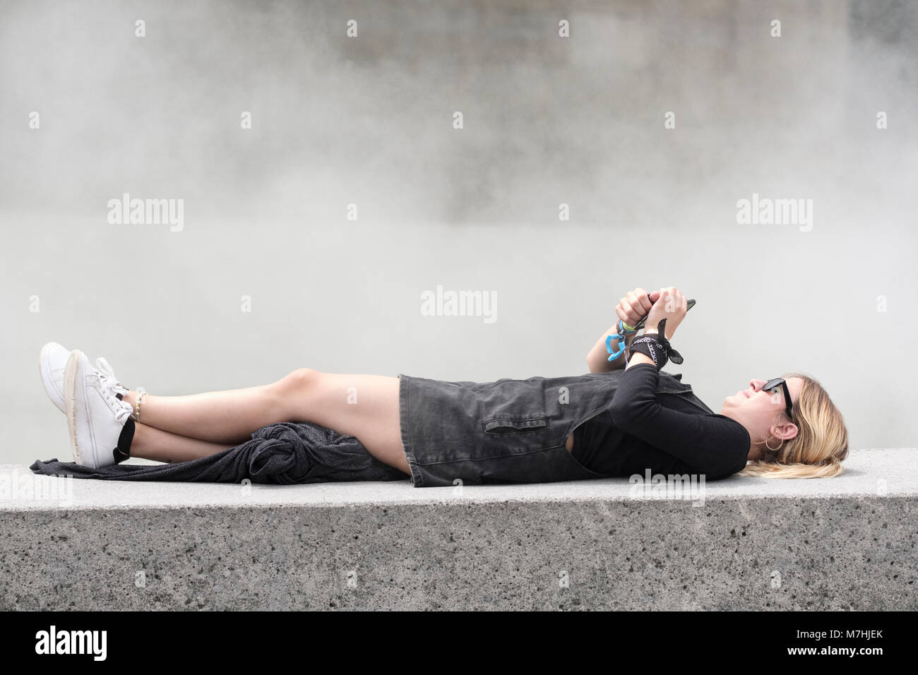 Jeune femme blonde avec queue de cheval, couché sur mur avec téléphone mobile, Bilbao, Vizcaya, Pays Basque, Espagne, Banque D'Images