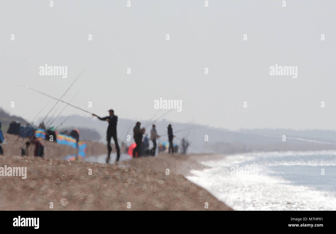 Les pêcheurs à la ligne dans une brume de chaleur sur une chaude journée sur la plage de Chesil UK, principalement la pêche du maquereau Banque D'Images